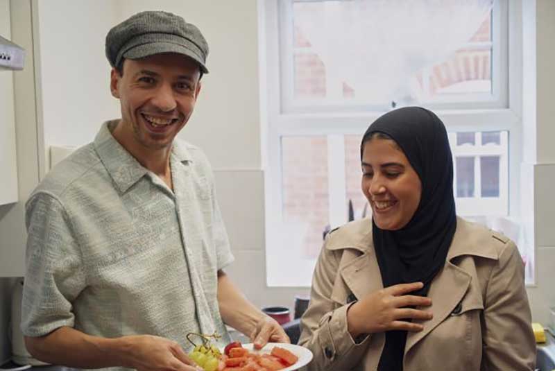 Man and woman holding plate of food in a kitchen