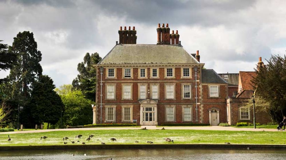 Forty Hall House with the grounds and lake in front .Geese are on the lawn. 