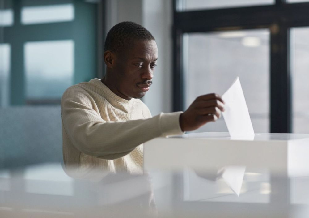 Man putting a folded vote in a clear ballot box