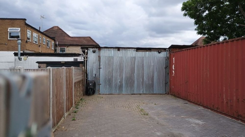 A paved area resembling a driveway surrounded by two large containers on an allotment