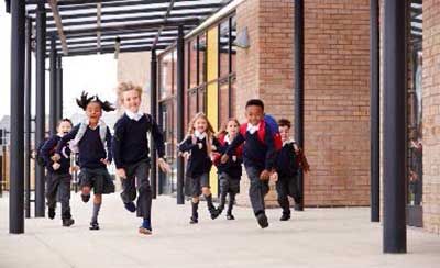 Children in school uniform running next to school building