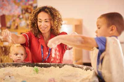 2 young children supervised by teacher playing with sand