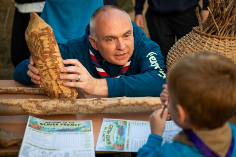 Beaver scouts leader talks to beavers while holding a log chewed by animals