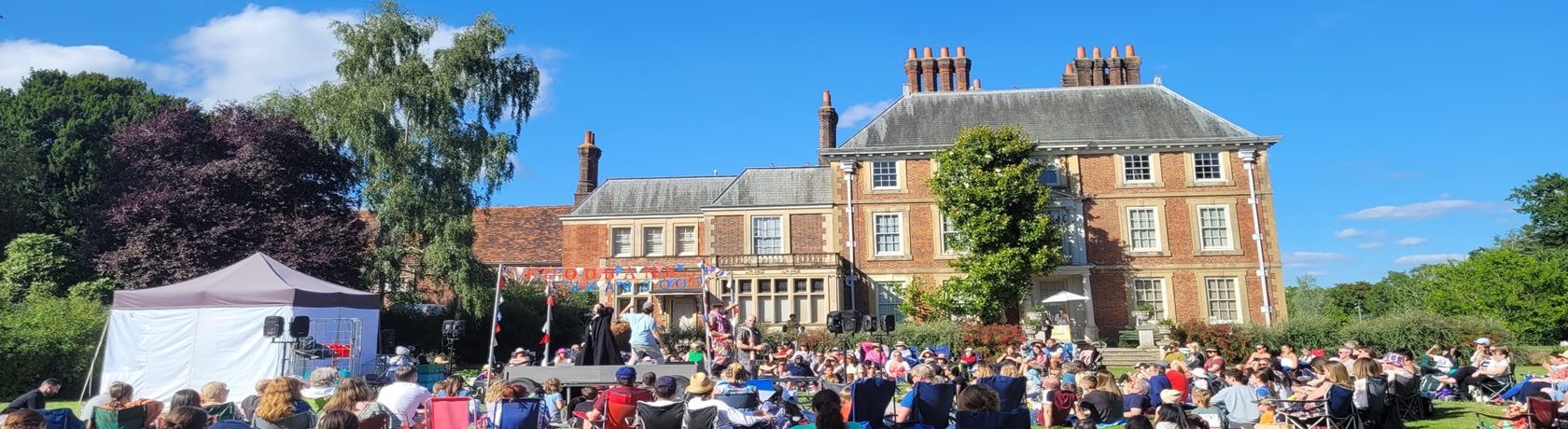 A crowd watching a play being performed on the lawn of Forty Hall