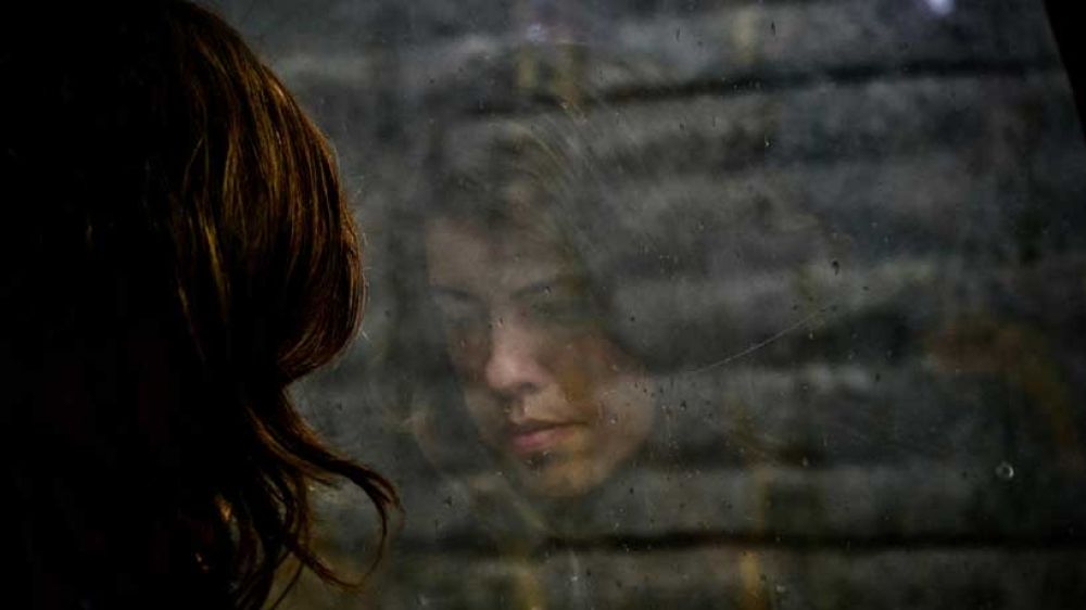 Woman gazes at her reflection in a window