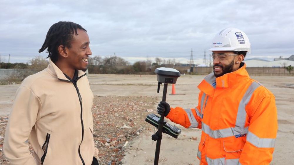 Two apprentices with surveying equipment smile at each other