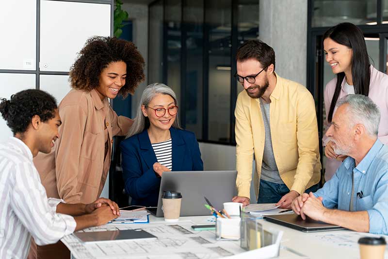 6 people round a table smiling and looking at a laptop