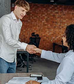 Teenage boy shaking hands with a lady sitting down at a desk