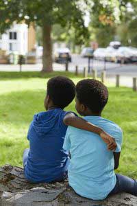 A child sitting in a park with his arm around another child 