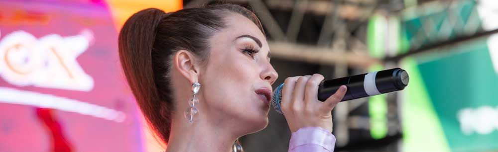 Young beautiful woman singing into a microphone in the style of Arianna Grande wearing pink outfit