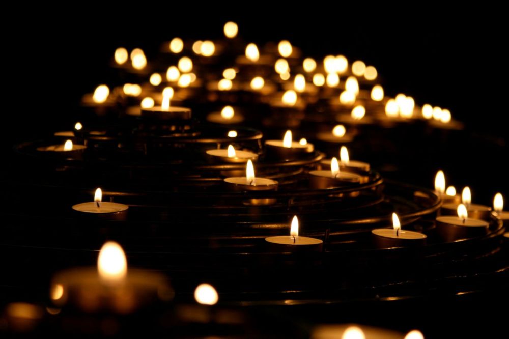 Rows of lit tea lights in sharp focus in the foreground and fading into the background
