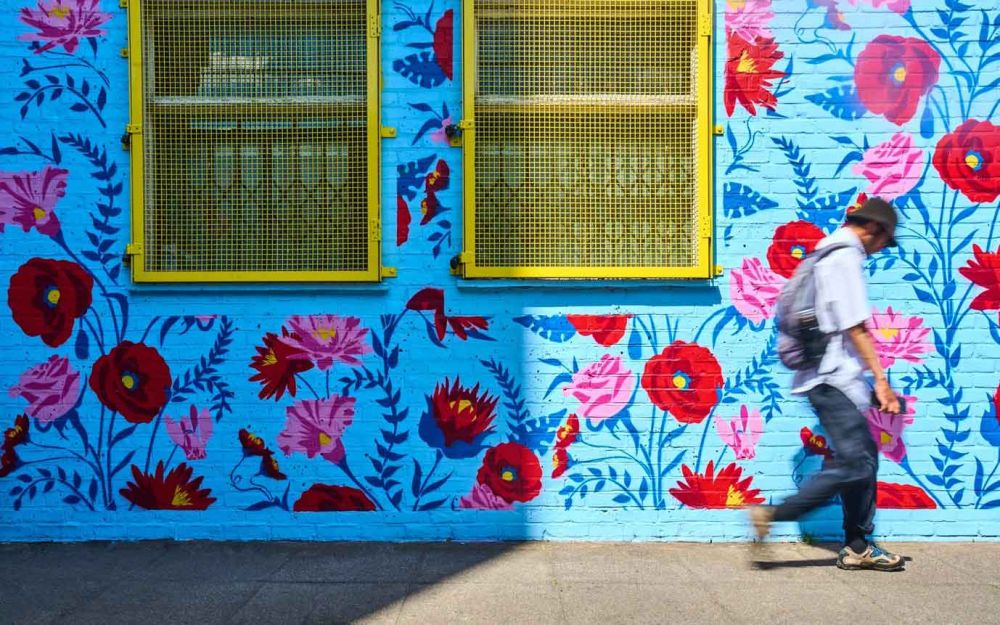Blurred image of man passing by a mural of  brightly coloured flowers and plants
