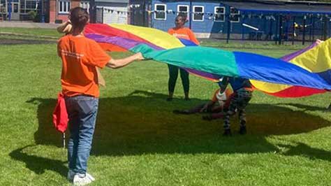 3 teenagers standing on grass and holding a colourful sheet