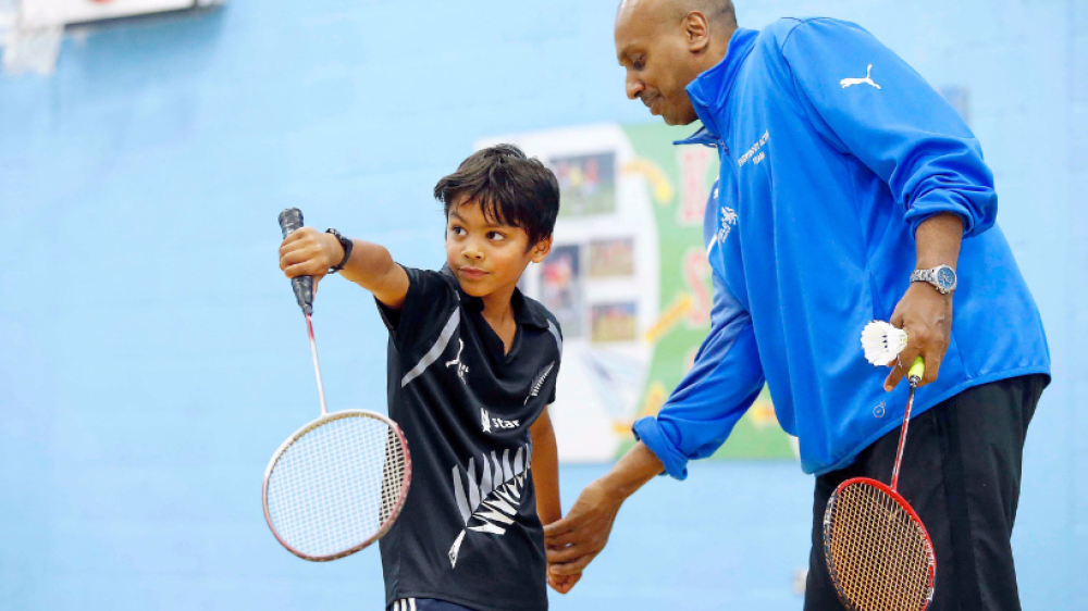 A young badminton player being coached by an adult