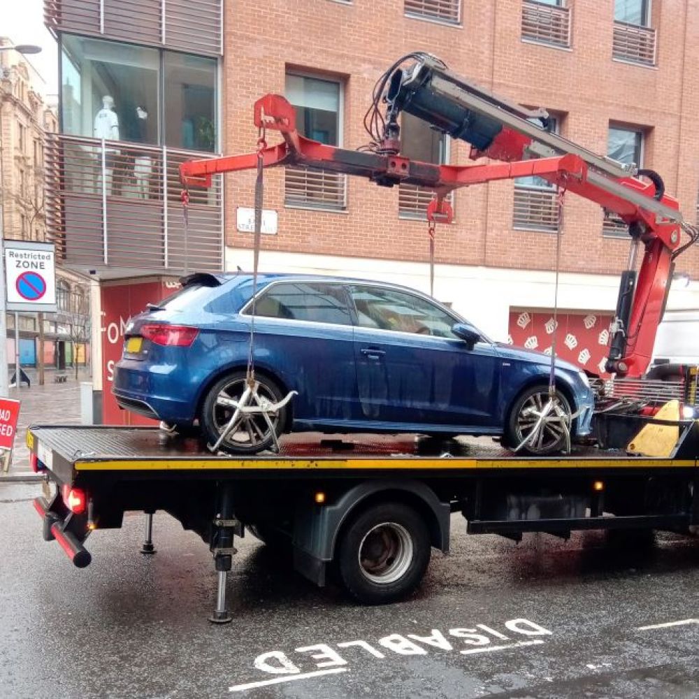 A car being lifted onto a trailer for misuse of a blue badge. A disabled parking bay is marked on the road